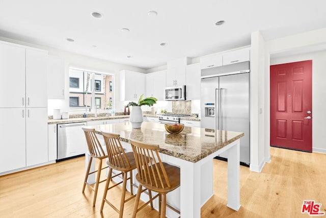 kitchen featuring white cabinetry, high end appliances, a center island, and dark stone countertops