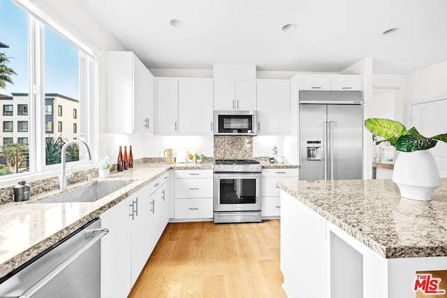 kitchen with sink, light hardwood / wood-style flooring, stainless steel appliances, light stone countertops, and white cabinets