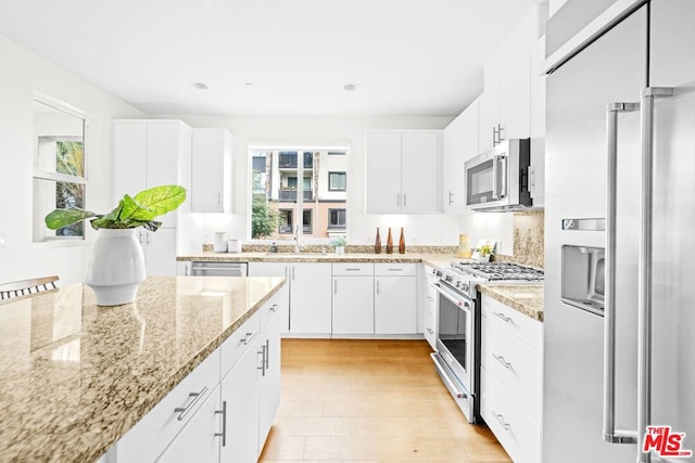 kitchen with white cabinetry, high quality appliances, light stone countertops, and a wealth of natural light