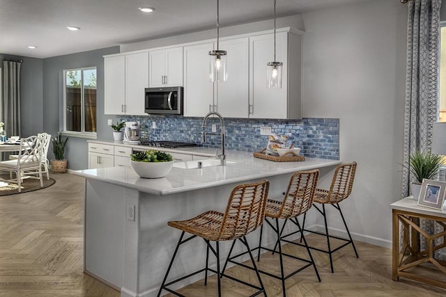 kitchen with decorative light fixtures, a breakfast bar area, white cabinets, light parquet floors, and stainless steel appliances