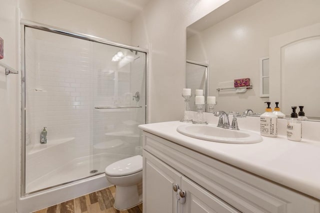 bathroom with hardwood / wood-style flooring, walk in shower, vanity, and toilet