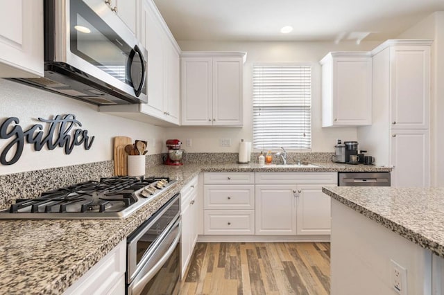 kitchen featuring sink, light hardwood / wood-style flooring, stainless steel appliances, light stone countertops, and white cabinets