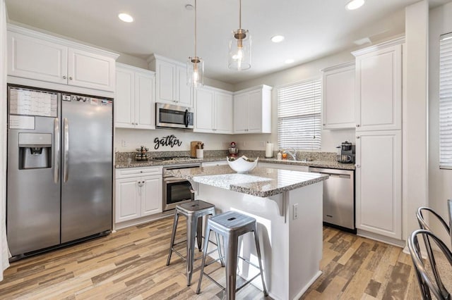 kitchen featuring white cabinetry, stainless steel appliances, decorative light fixtures, and a kitchen island