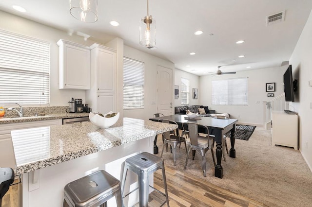 kitchen featuring sink, light stone counters, hanging light fixtures, a kitchen breakfast bar, and white cabinets