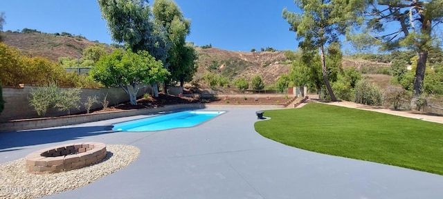 view of swimming pool featuring a patio, an outdoor fire pit, a mountain view, and a lawn