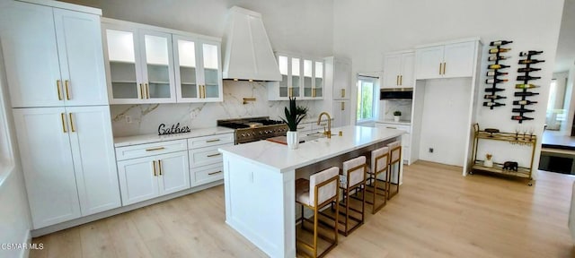 kitchen with premium range hood, a breakfast bar area, white cabinetry, a center island with sink, and double oven range