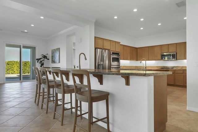 kitchen featuring sink, a breakfast bar, stainless steel appliances, ornamental molding, and an island with sink