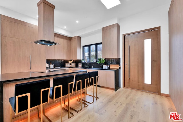 kitchen with island exhaust hood, light brown cabinets, and decorative backsplash