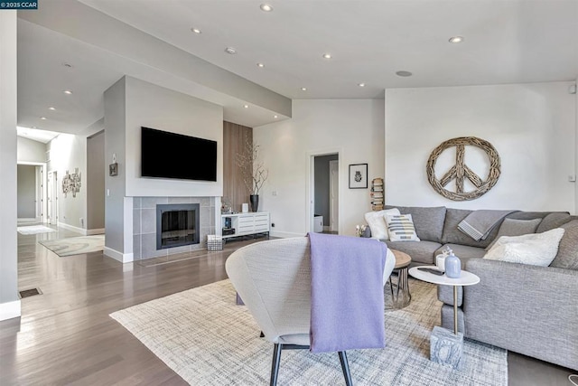 living room with a tile fireplace, vaulted ceiling, and hardwood / wood-style floors