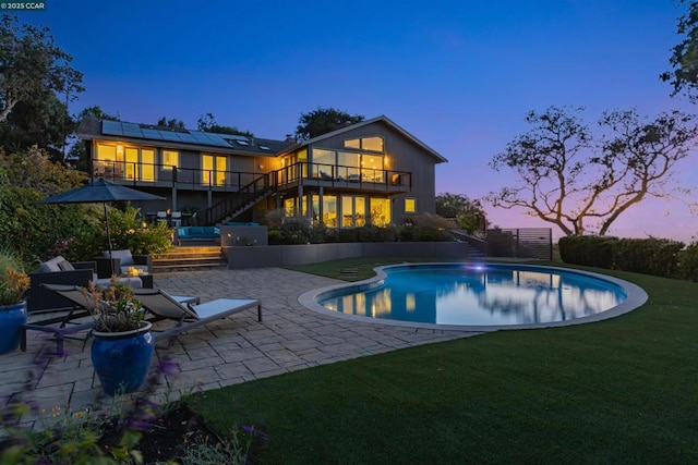 back house at dusk with a lawn, a patio area, and solar panels