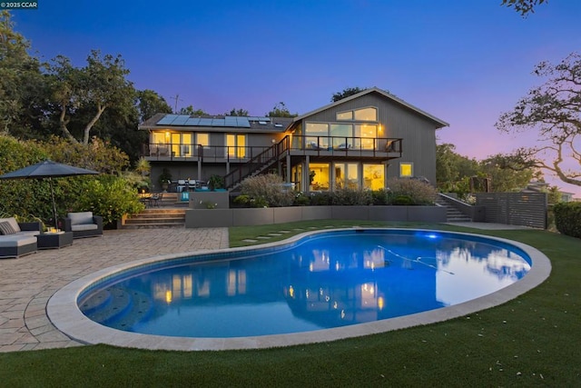 back house at dusk featuring a balcony, a patio, and solar panels