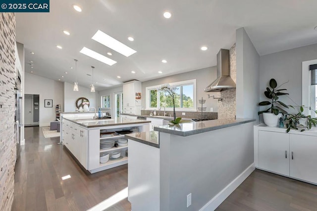 kitchen with pendant lighting, wall chimney exhaust hood, kitchen peninsula, and white cabinets