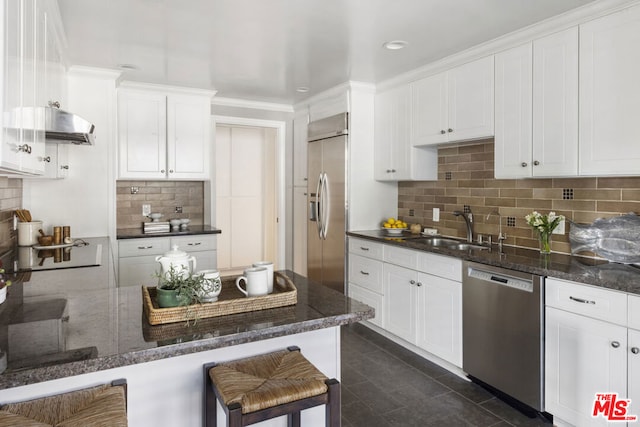 kitchen with sink, dark stone countertops, stainless steel appliances, white cabinets, and a kitchen bar