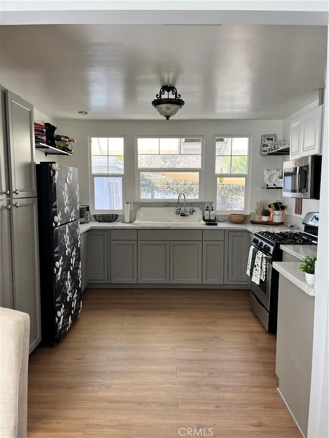 kitchen with stainless steel appliances, sink, light hardwood / wood-style floors, and gray cabinetry