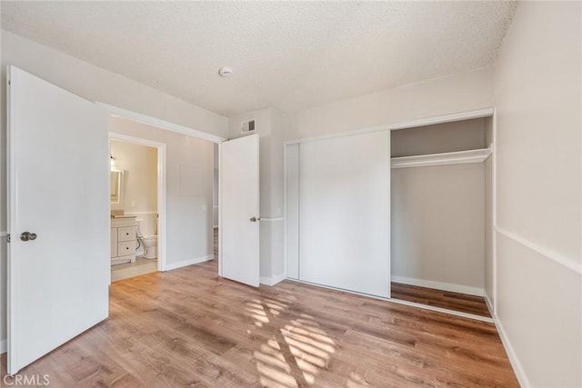 unfurnished bedroom with hardwood / wood-style flooring, ensuite bathroom, a textured ceiling, and a closet