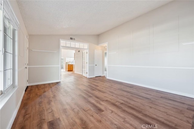 unfurnished room featuring lofted ceiling, wood-type flooring, and a textured ceiling