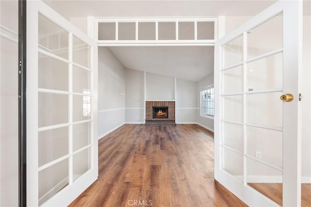 unfurnished living room featuring lofted ceiling, a brick fireplace, and hardwood / wood-style flooring