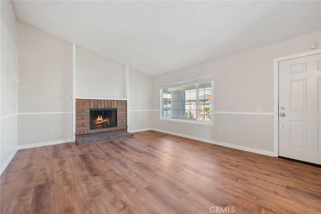 unfurnished living room featuring lofted ceiling, a brick fireplace, and wood-type flooring