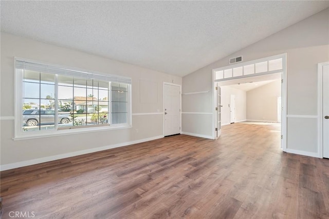 empty room featuring wood-type flooring, vaulted ceiling, and a textured ceiling