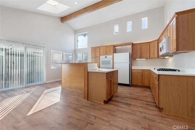 kitchen with a center island, a skylight, light hardwood / wood-style flooring, beamed ceiling, and white appliances