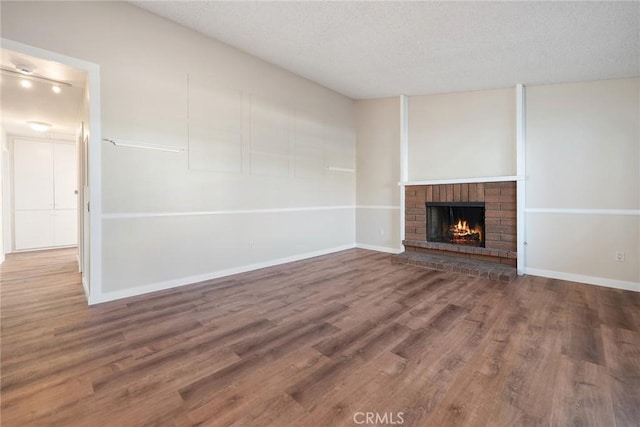 unfurnished living room featuring a brick fireplace, wood-type flooring, and a textured ceiling