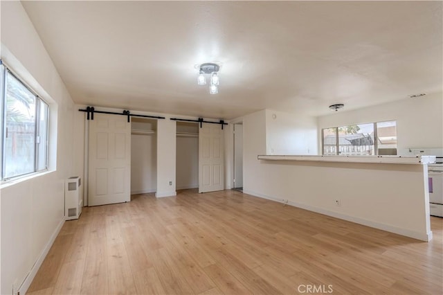 unfurnished bedroom featuring multiple windows, a barn door, radiator, and light wood-type flooring