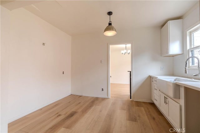 kitchen featuring hanging light fixtures, white cabinetry, sink, and light wood-type flooring