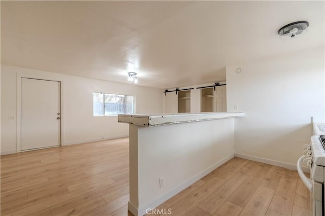 interior space featuring stove, light hardwood / wood-style floors, kitchen peninsula, and a barn door