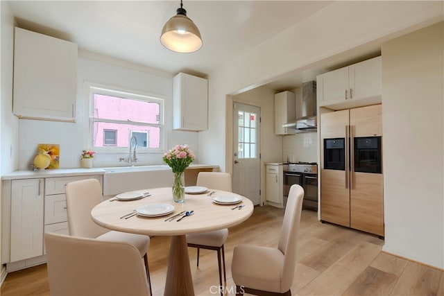 kitchen featuring sink, white cabinetry, hanging light fixtures, paneled built in fridge, and wall chimney exhaust hood