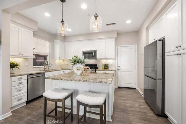 kitchen with appliances with stainless steel finishes, a kitchen island, white cabinetry, hanging light fixtures, and dark wood-type flooring