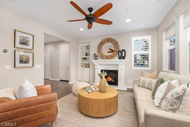 living room featuring built in shelves, wood-type flooring, and ceiling fan