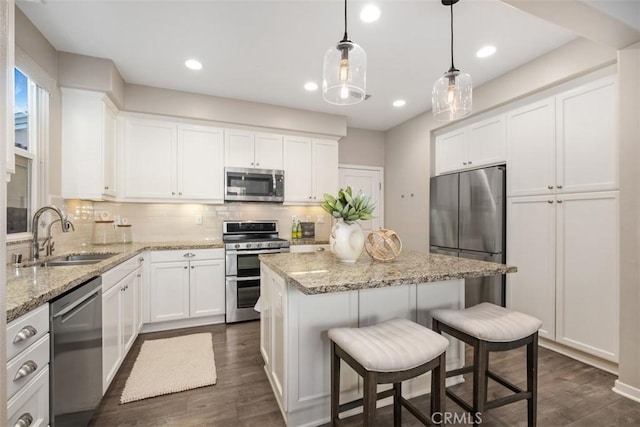 kitchen with appliances with stainless steel finishes, pendant lighting, white cabinetry, sink, and a center island