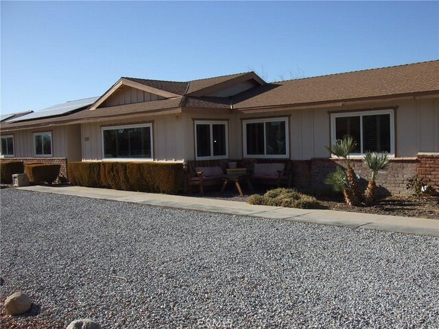 ranch-style house featuring board and batten siding, solar panels, and brick siding