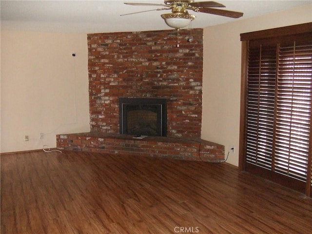 unfurnished living room with wood finished floors, ceiling fan, and a brick fireplace