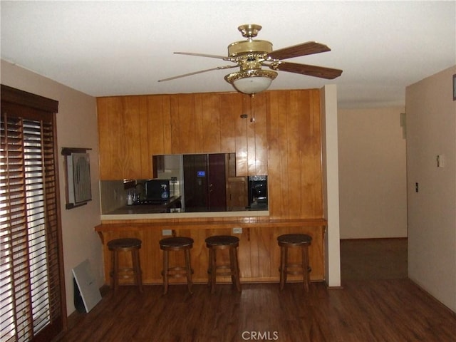 kitchen featuring dark wood-style flooring, brown cabinets, ceiling fan, a kitchen breakfast bar, and tile counters