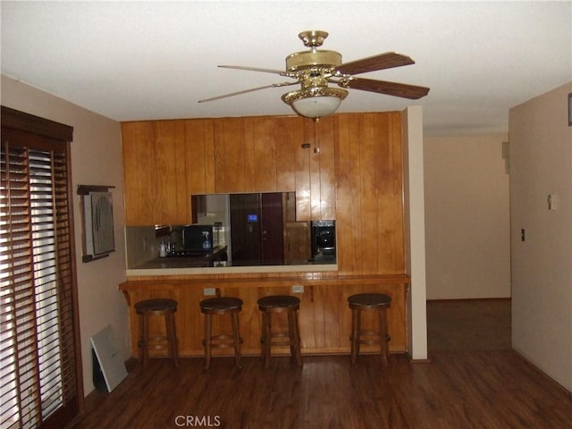 kitchen with brown cabinetry, dark wood finished floors, a ceiling fan, a breakfast bar area, and tile countertops