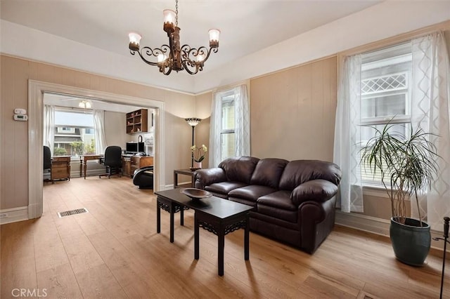 living room featuring baseboards, light wood-type flooring, visible vents, and a notable chandelier