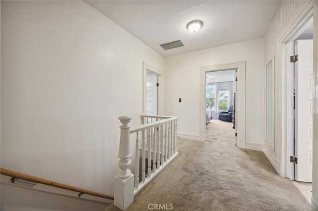 hallway with visible vents, baseboards, light colored carpet, and an upstairs landing