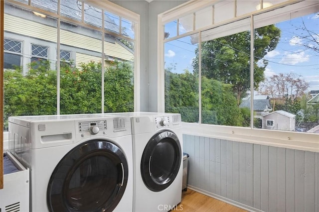 clothes washing area featuring light hardwood / wood-style flooring, wooden walls, and washing machine and clothes dryer