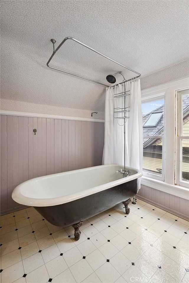 full bathroom with a textured ceiling, curtained shower, a freestanding tub, wainscoting, and tile patterned floors