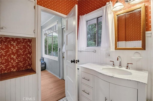 bathroom with wood finished floors, vanity, and wallpapered walls