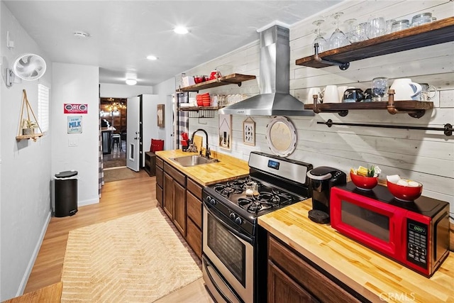 kitchen with island range hood, sink, backsplash, gas stove, and light hardwood / wood-style flooring