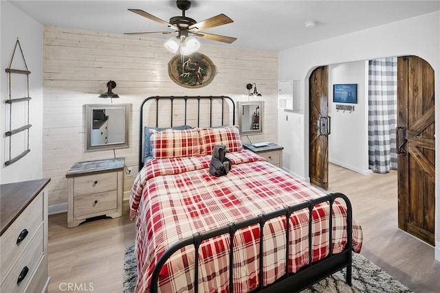 bedroom with wooden walls, light hardwood / wood-style floors, and ceiling fan