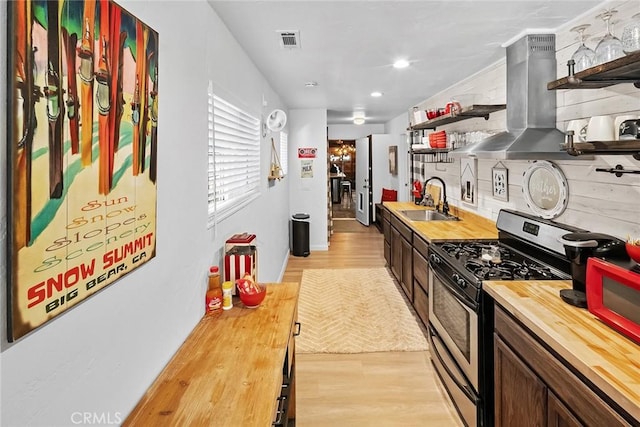 kitchen featuring sink, wooden counters, light wood-type flooring, stainless steel range with gas cooktop, and island exhaust hood