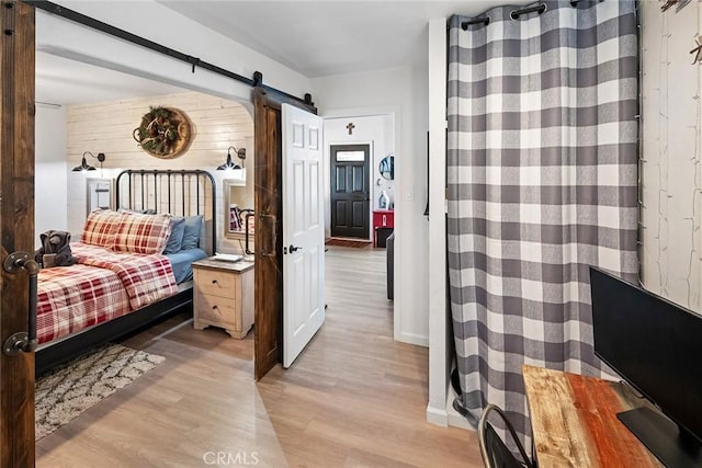 bedroom featuring a barn door, light hardwood / wood-style floors, and wood walls