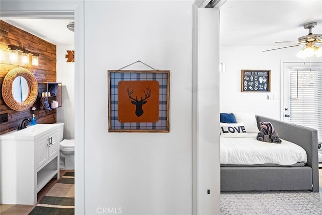 bedroom featuring sink, ensuite bathroom, ceiling fan, and wood walls