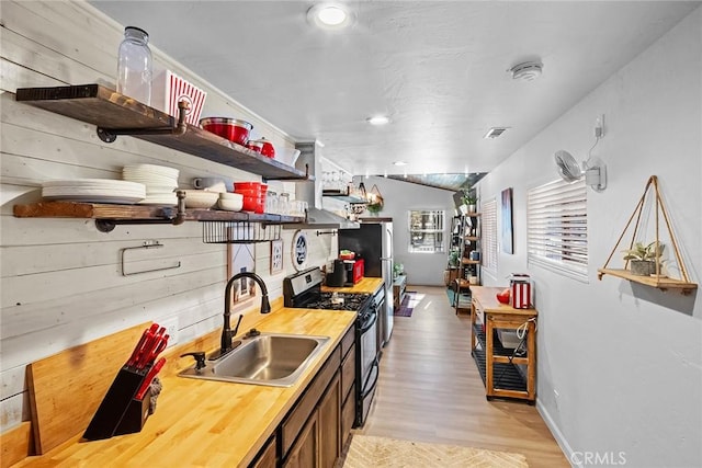 kitchen with lofted ceiling, sink, light hardwood / wood-style flooring, and stainless steel gas range oven