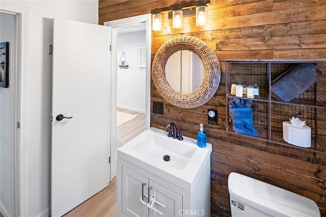 bathroom with toilet, vanity, and wooden walls