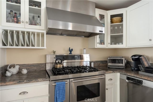 kitchen with white cabinetry, extractor fan, stainless steel appliances, and dark stone countertops