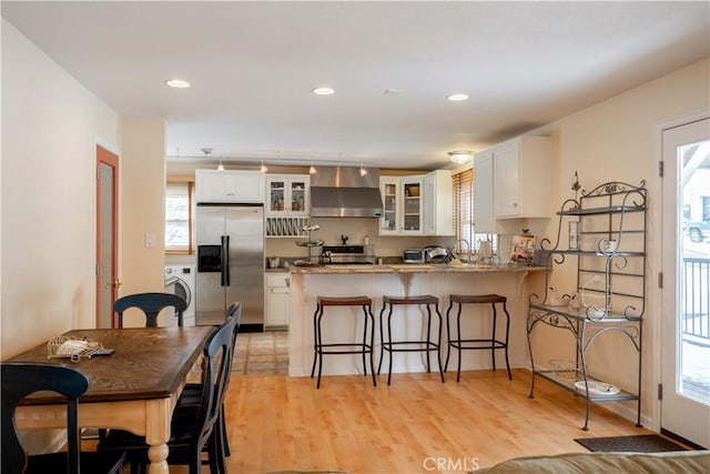 kitchen with white cabinetry, wall chimney exhaust hood, washer / dryer, and stainless steel fridge with ice dispenser